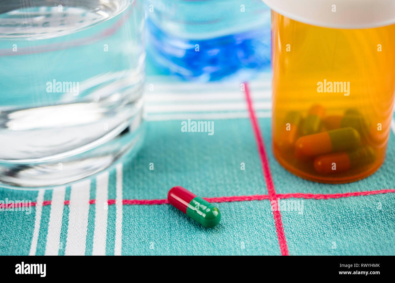 Medicazione durante la colazione, capsule accanto ad un bicchiere di acqua, immagine concettuale, composizione orizzontale Foto Stock