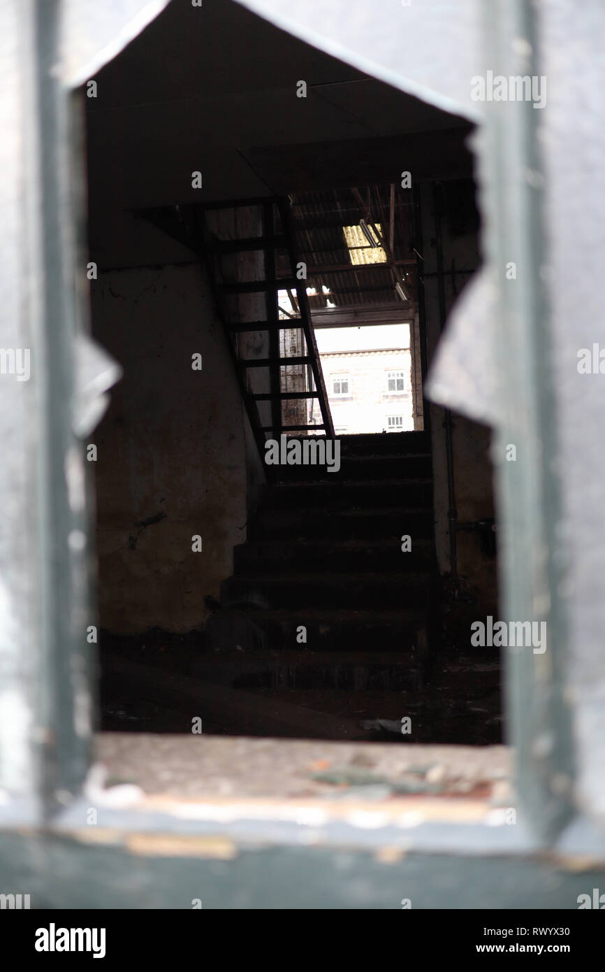 Il peering attraverso un vetro rotto in un edificio abbandonato. Foto Stock