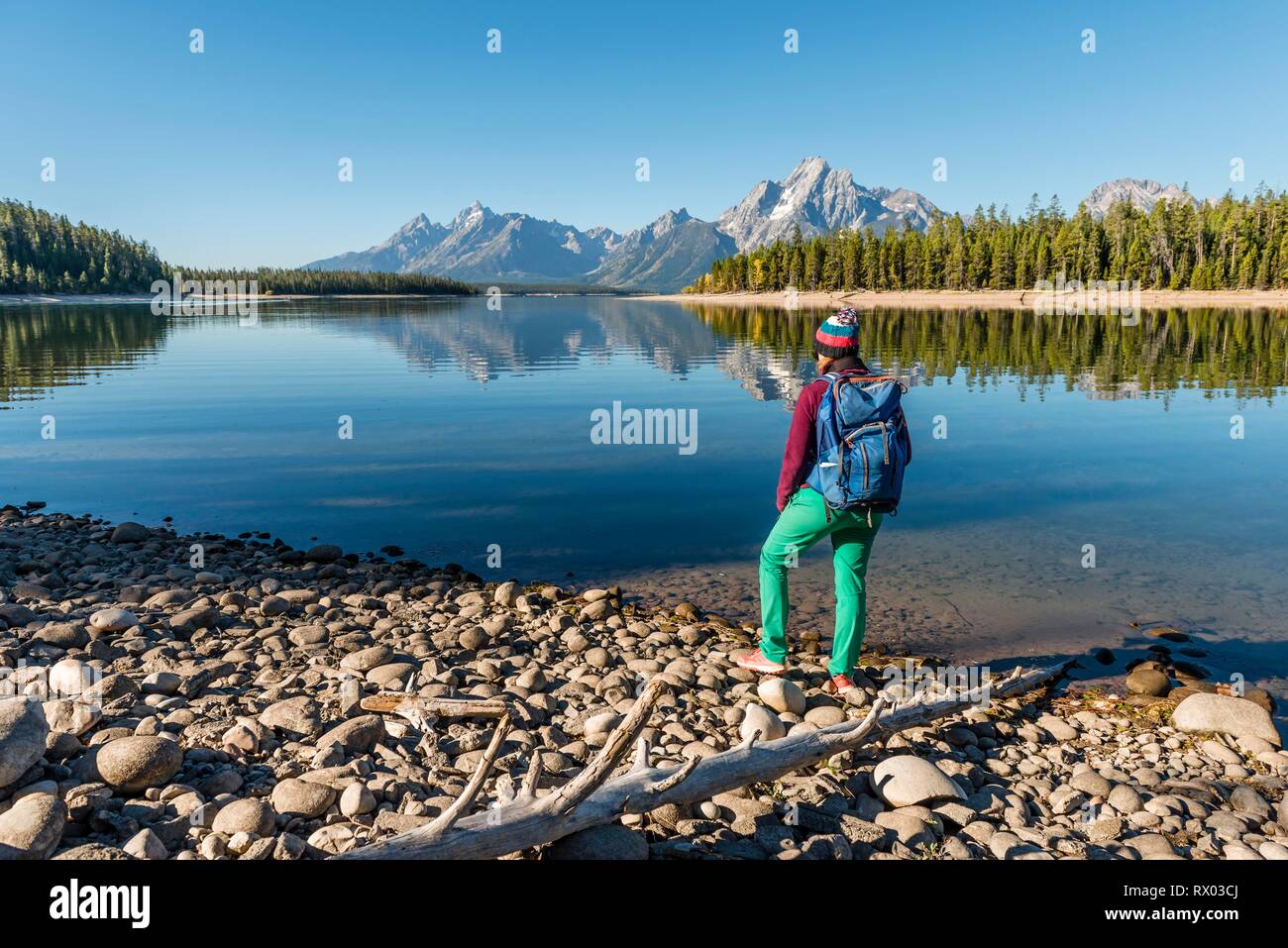 Giovane donna con zaino in piedi sulla riva, montagne riflesse nel lago, Colter Bay, il lago Jackson, Teton gamma Foto Stock