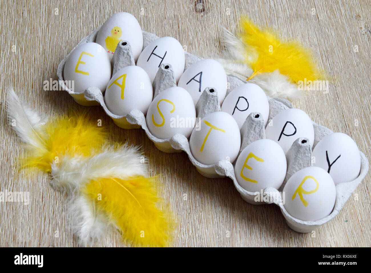 Felice Pasqua scritto su bianco uova in una scatola e piume di colore giallo su sfondo di legno Foto Stock
