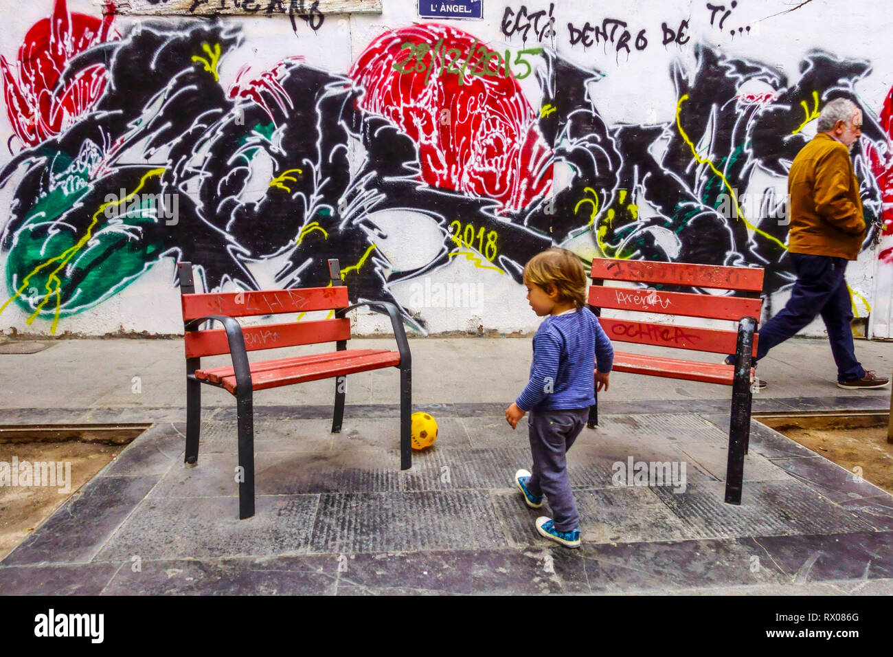 Vista sulla strada, UN bambino che gioca con una palla e un uomo che passa intorno a colorati muri di graffiti, Valencia, quartiere della città vecchia di El Carmen Foto Stock