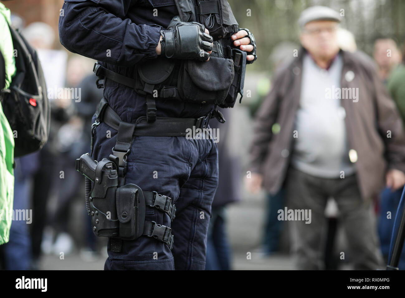 Dettagli del kit di protezione di un riot police officer (comprese le manette, 9mm pistola, stazione radio e testimone) seduto tra i civili Foto Stock