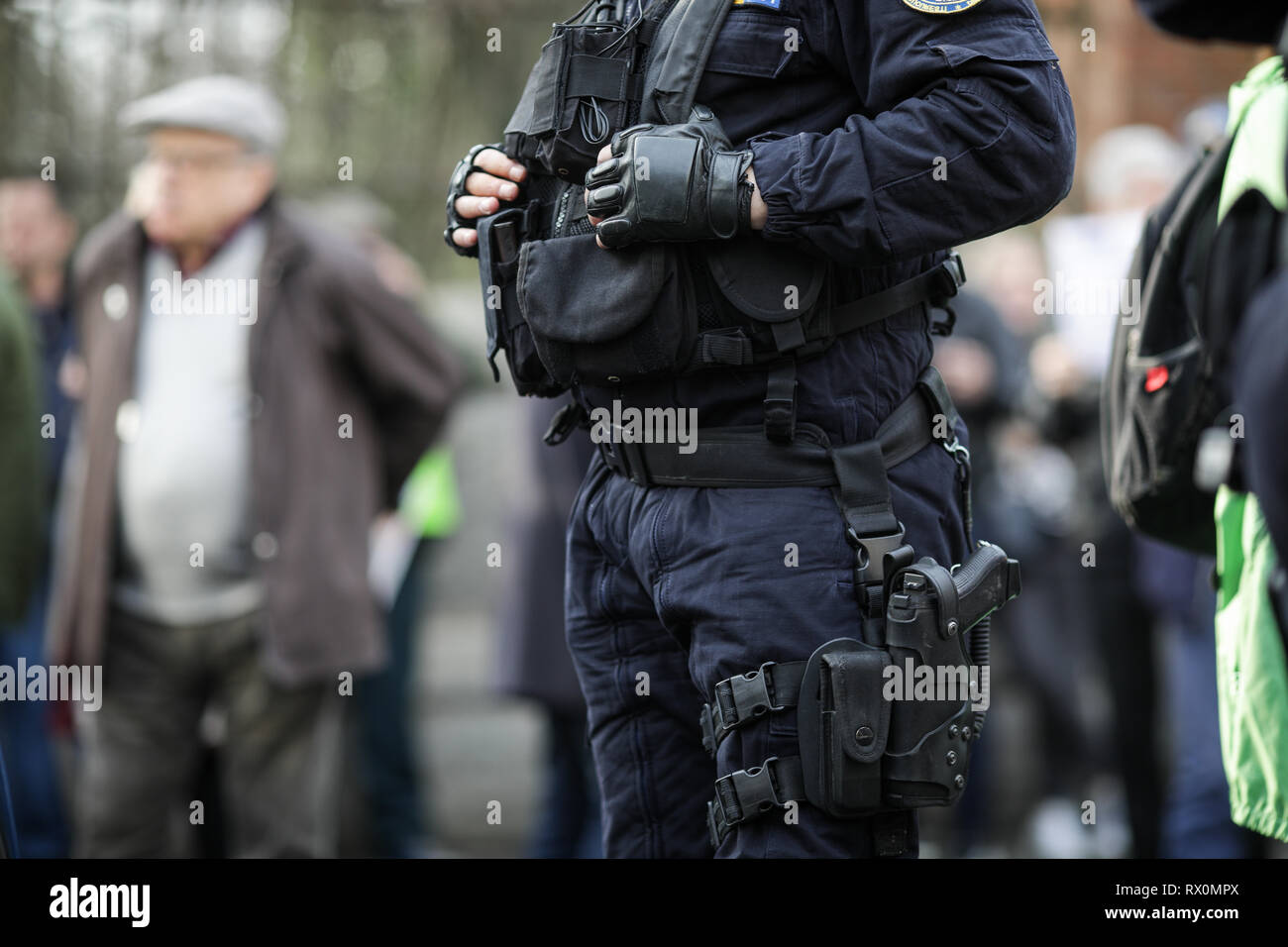 Dettagli del kit di protezione di un riot police officer (comprese le manette, 9mm pistola, stazione radio e testimone) seduto tra i civili Foto Stock