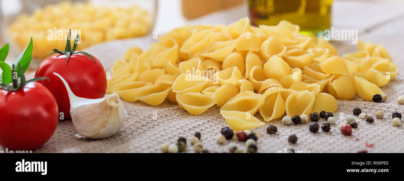 Il cibo italiano preparazione. Forma a guscio di pasta, pomodori, aglio e pepe semi, banner Foto Stock