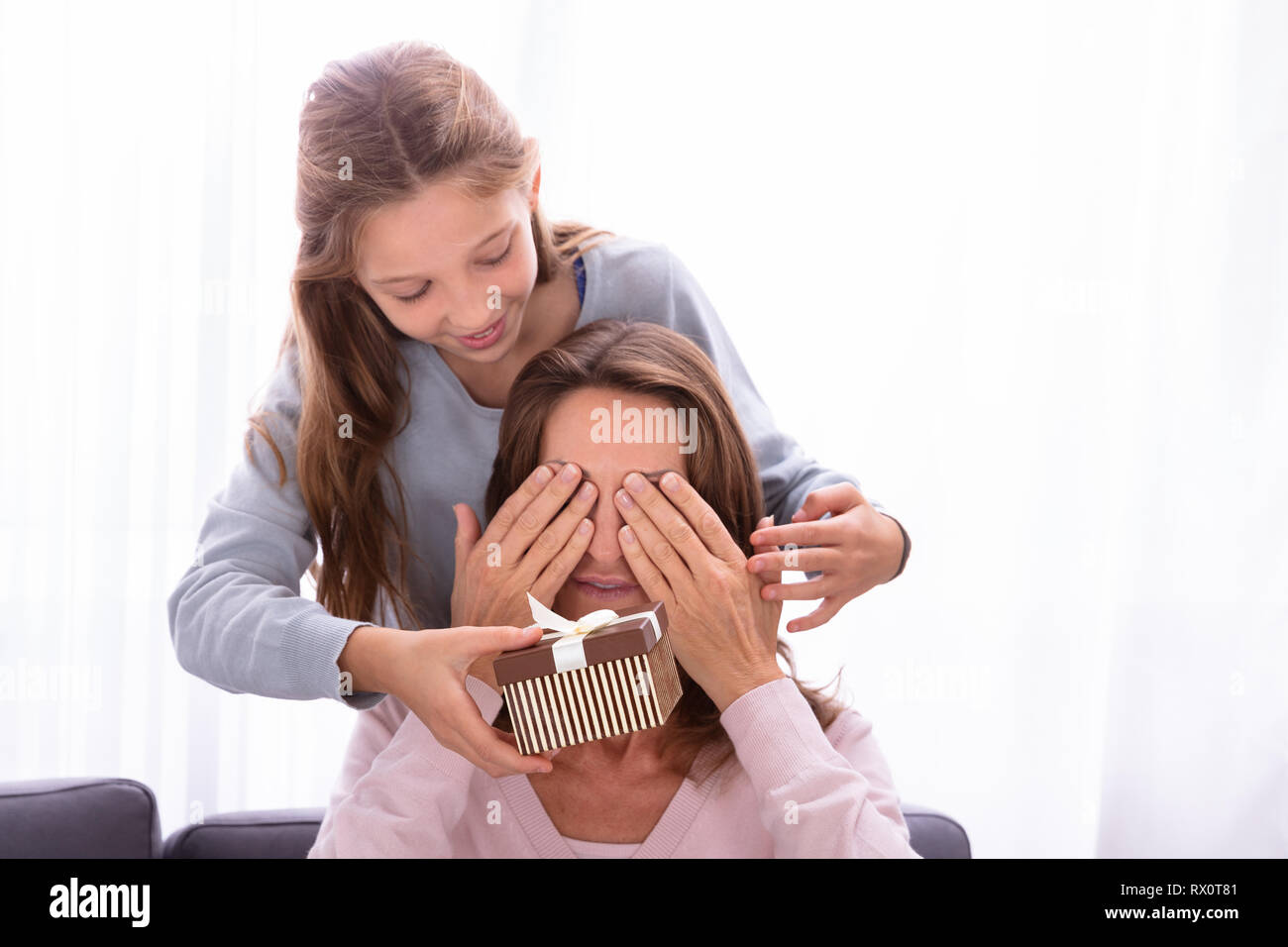 Close-up di ragazza dando regalo a sorpresa per la madre che copre i suoi occhi Foto Stock