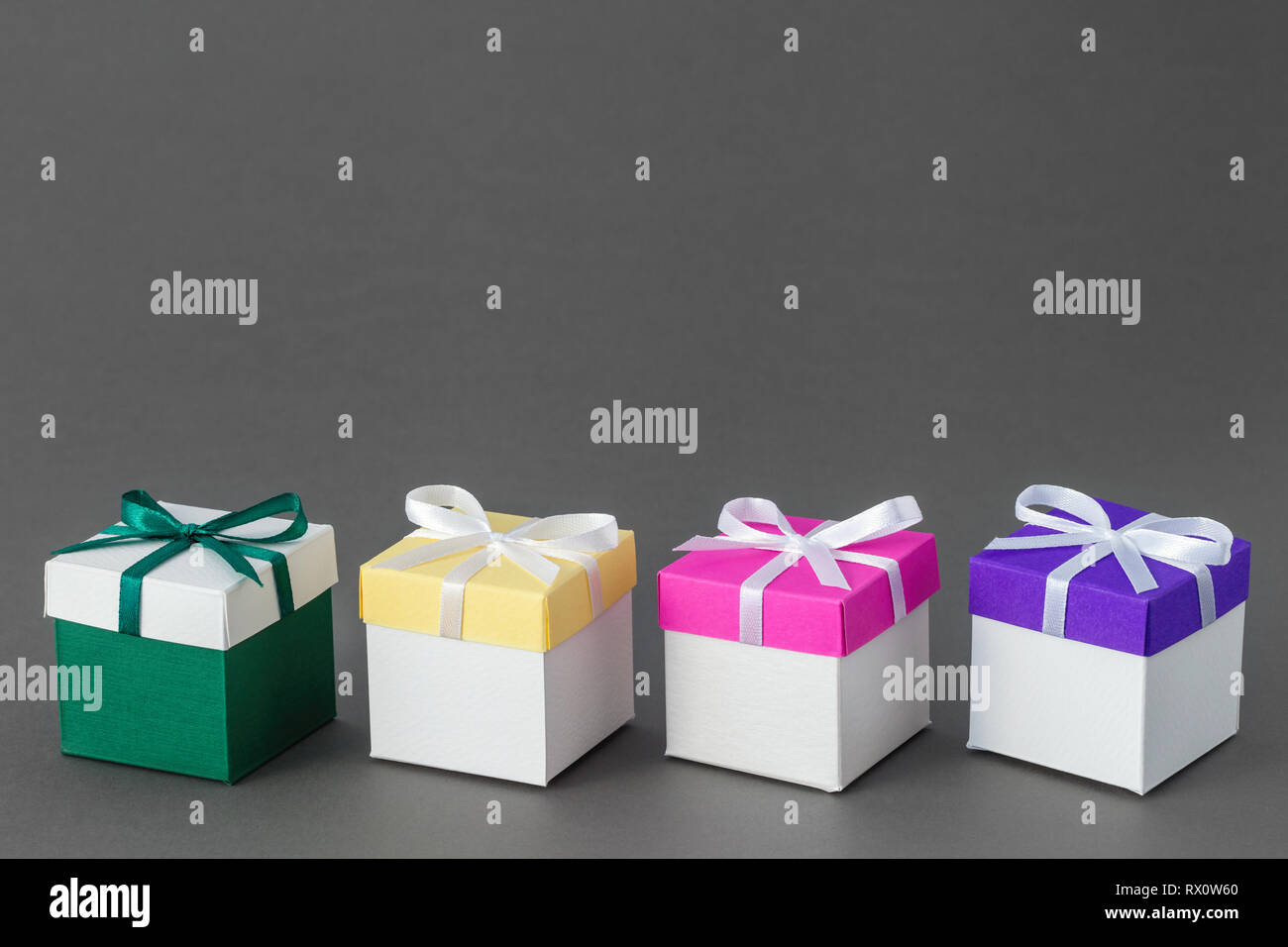 Quattro scatole regalo con nastri su sfondo grigio. Copia spazio per il testo. Foto Stock