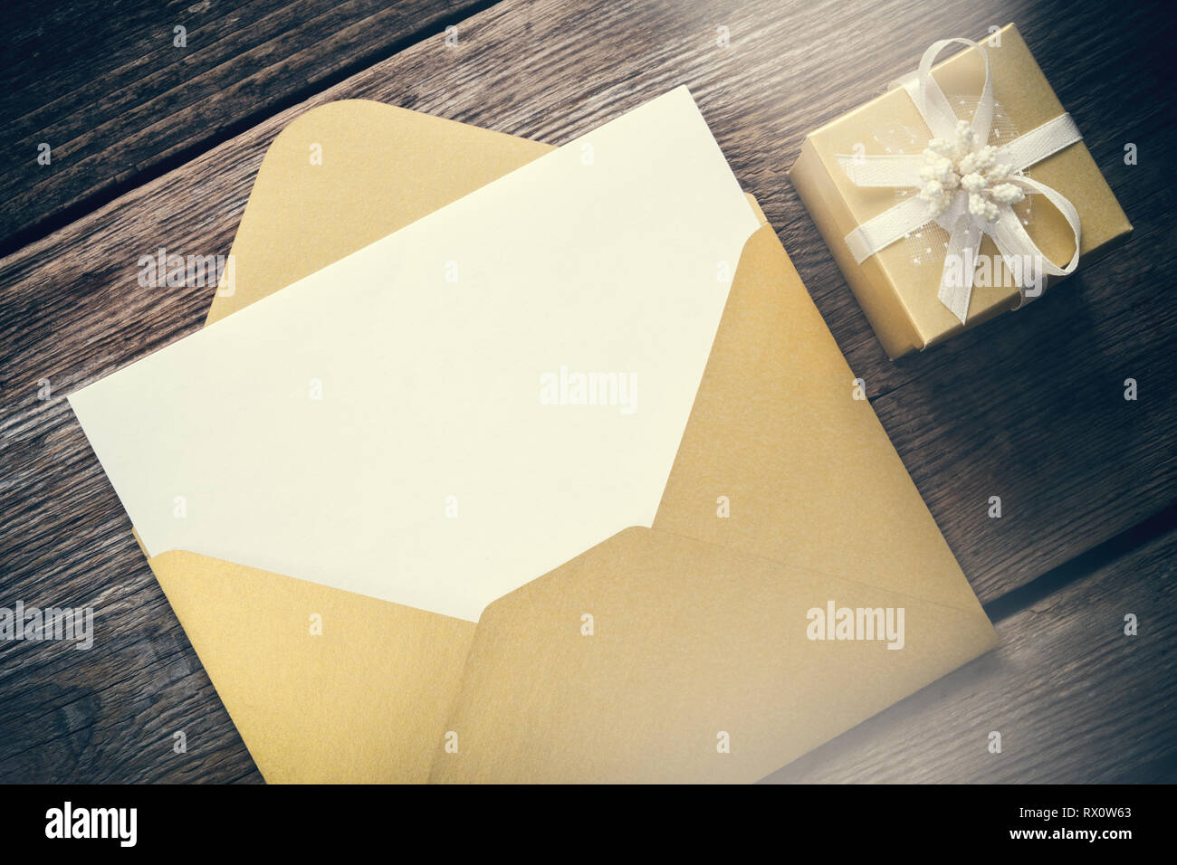 Aprire carta gialla busta vuota con foglio di carta e confezione regalo con nastro sul pannello di legno. Foto Stock