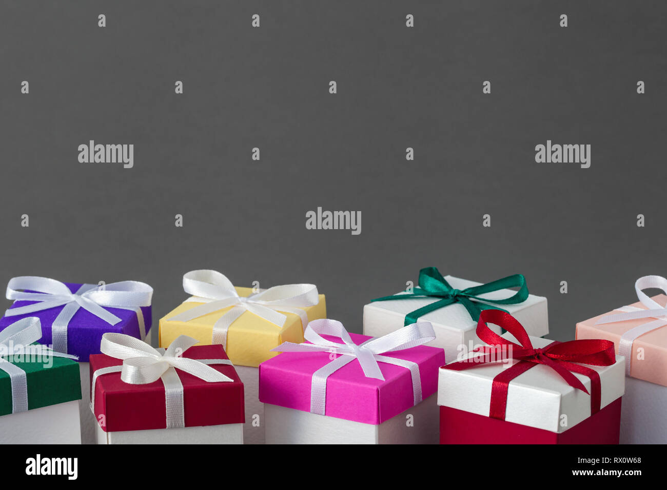 Varie confezioni regalo con luminosi coperchi colorati e nastri su sfondo grigio. Copia spazio per il testo. Foto Stock