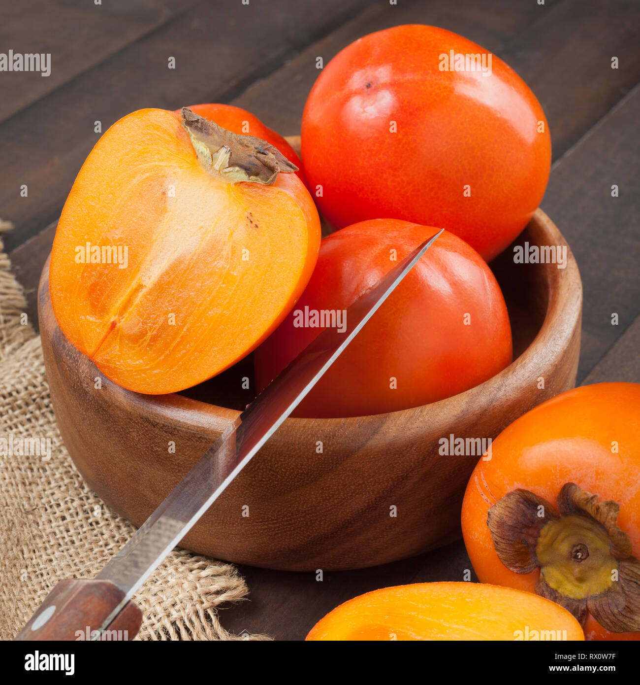 Cachi nella ciotola con il coltello da cucina su un tavolo di legno. Foto Stock