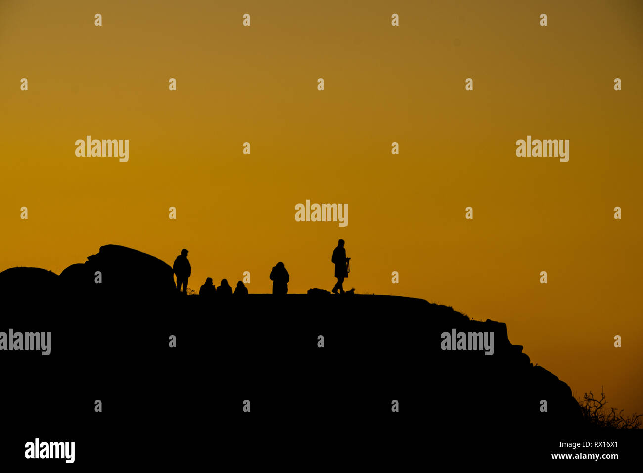 Silhouette di persone sulla cima di una montagna al tramonto con il cielo arancione Foto Stock