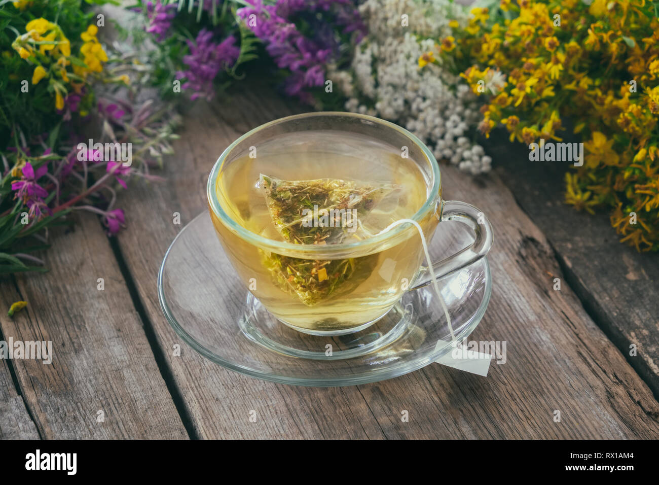 Vetro tazza di tè con un sacchetto da tè di sano tè alle erbe e grappoli di erbe medicinali su sfondo, non a fuoco. Foto Stock