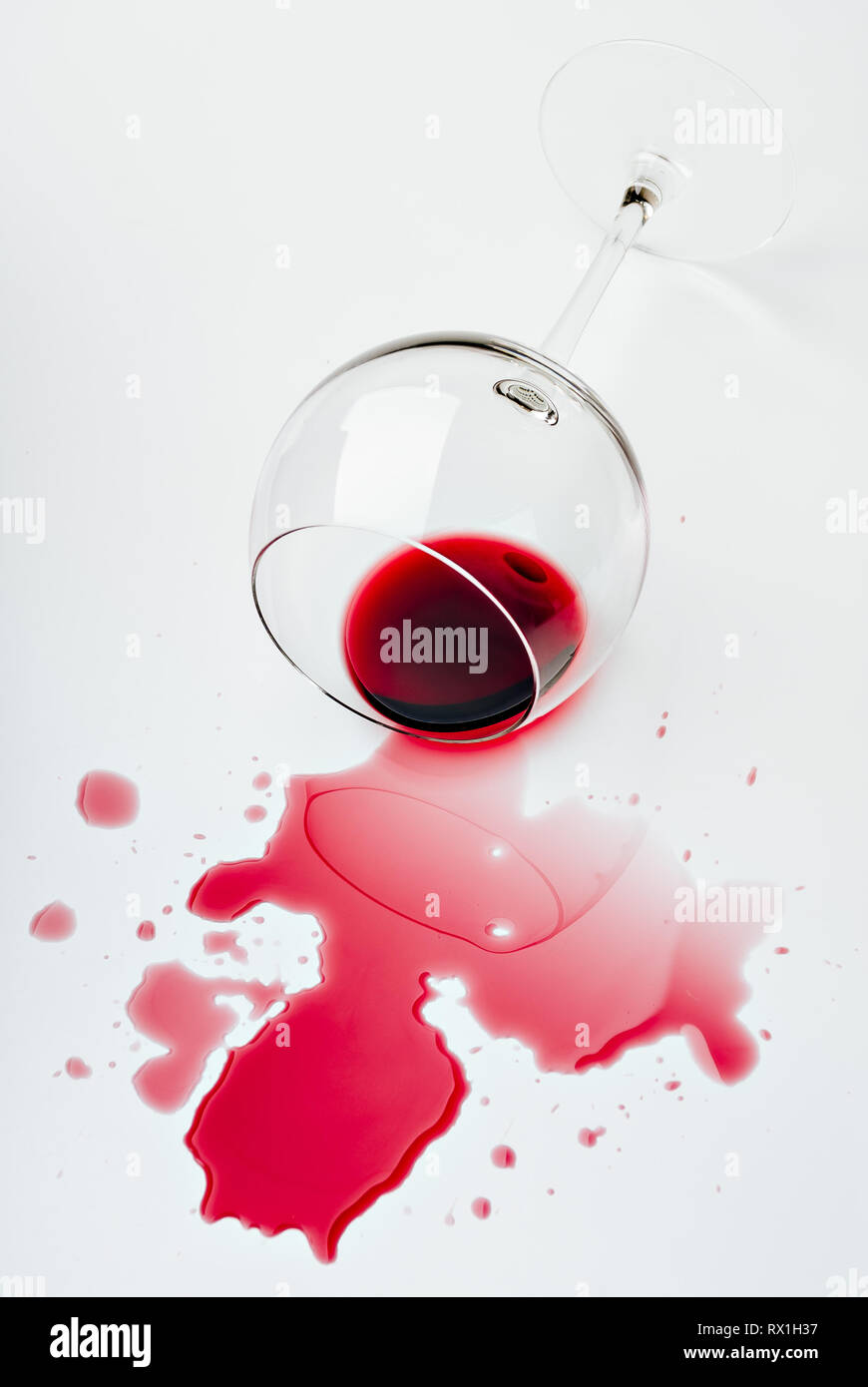 Rosso vino versato da un wineglass su una superficie bianca Foto Stock