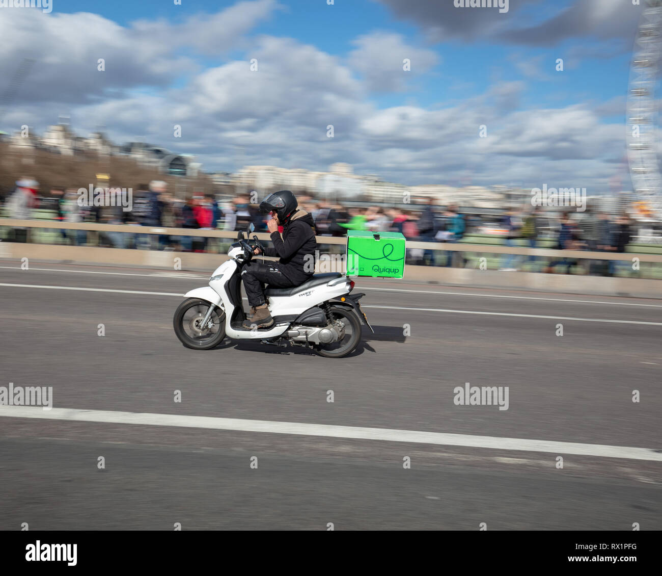 Un motociclista che consegna a domicilio viaggia velocemente sul Westminster Bridge, Londra, Regno Unito, in una giornata di marzo, fresca e mutevole. Foto Stock