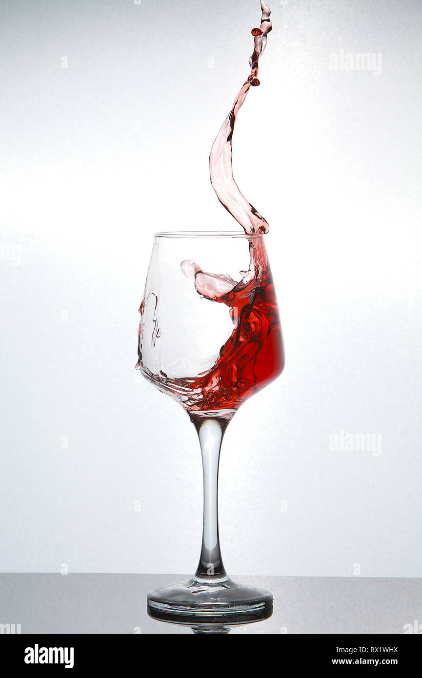 Close-up di vino rosso spruzzi in vetro su tavola contro uno sfondo bianco Foto Stock