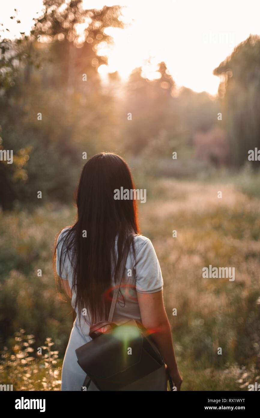 Vista posteriore della donna con zaino camminando sul campo erboso contro sky in park durante il tramonto Foto Stock