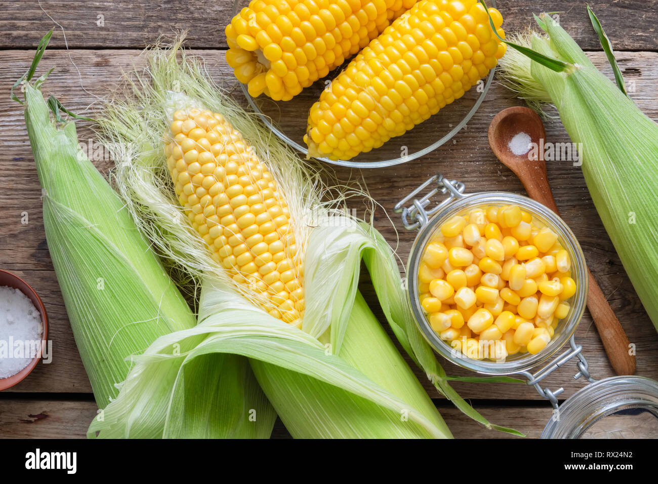 Conserve di mais dolce in un barattolo di vetro, fresco e grano cotto su pannocchie, sale. Vista dall'alto. Foto Stock
