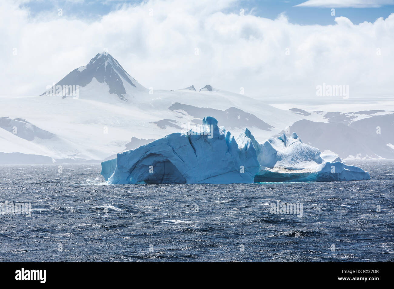 Un pinnacolo roccioso si erge alto dietro un iceberg che galleggia nello stretto di Bransfield all'interno della penisola antartica, dello stretto di Bransfield, della penisola antartica e dell'Antartide Foto Stock