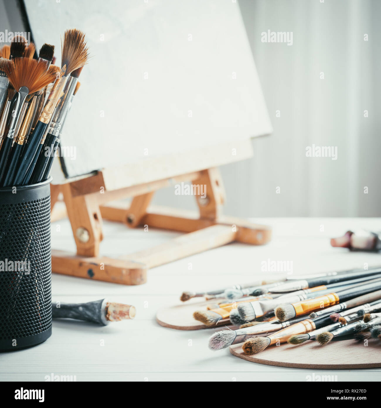 Attrezzature artistiche nel pittore studio: cavalletto, pennelli, tubi di vernice, tavolozza e dipinti su tavola di lavoro di artista. Foto Stock