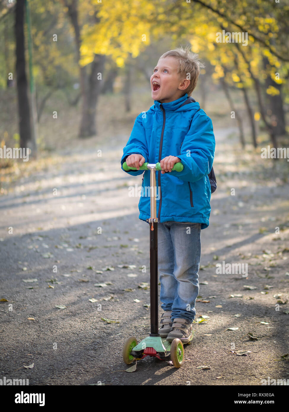 Un ragazzo in blu vestiti equitazione con un ampio sorriso su uno scooter in autunno park. Foto Stock