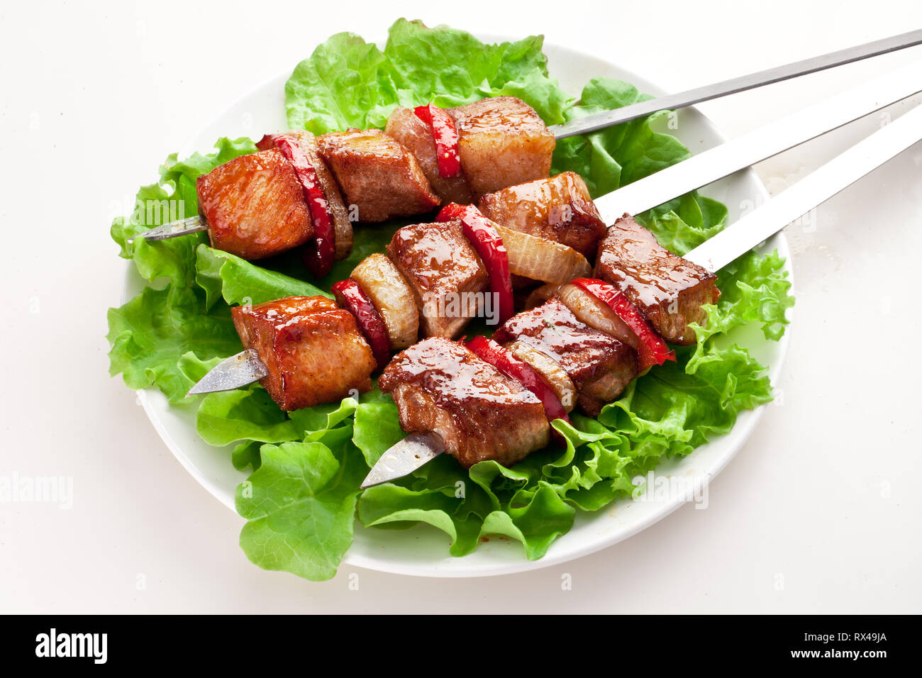 Grigliate di carne e verdure sopra le foglie verdi sulla piastra bianca. Foto Stock