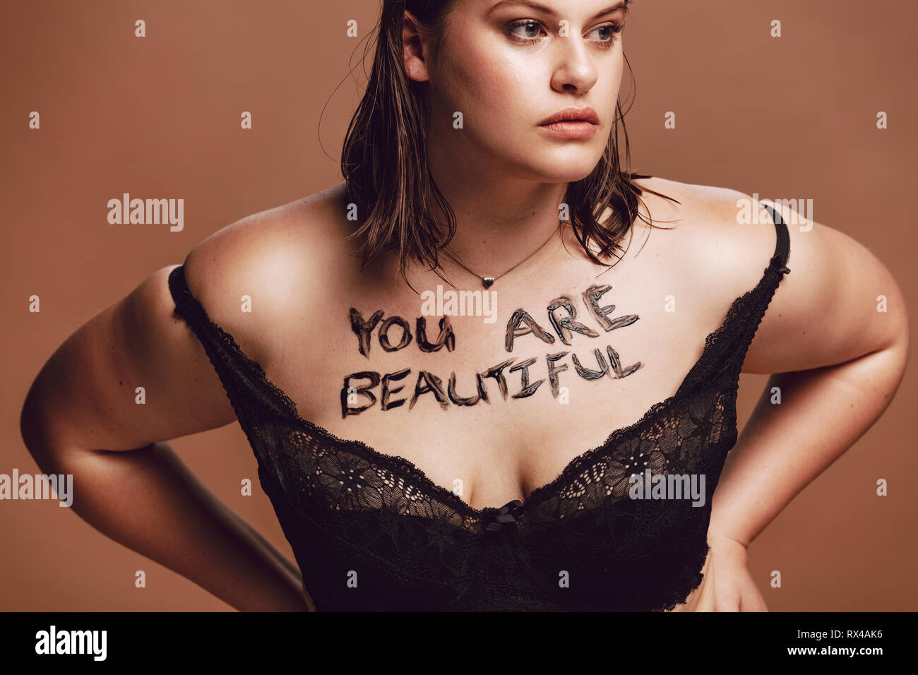 Femmina sovradimensionata nel reggiseno nero su sfondo marrone. Donna con parole " sei bella' scritta sul suo corpo. Foto Stock