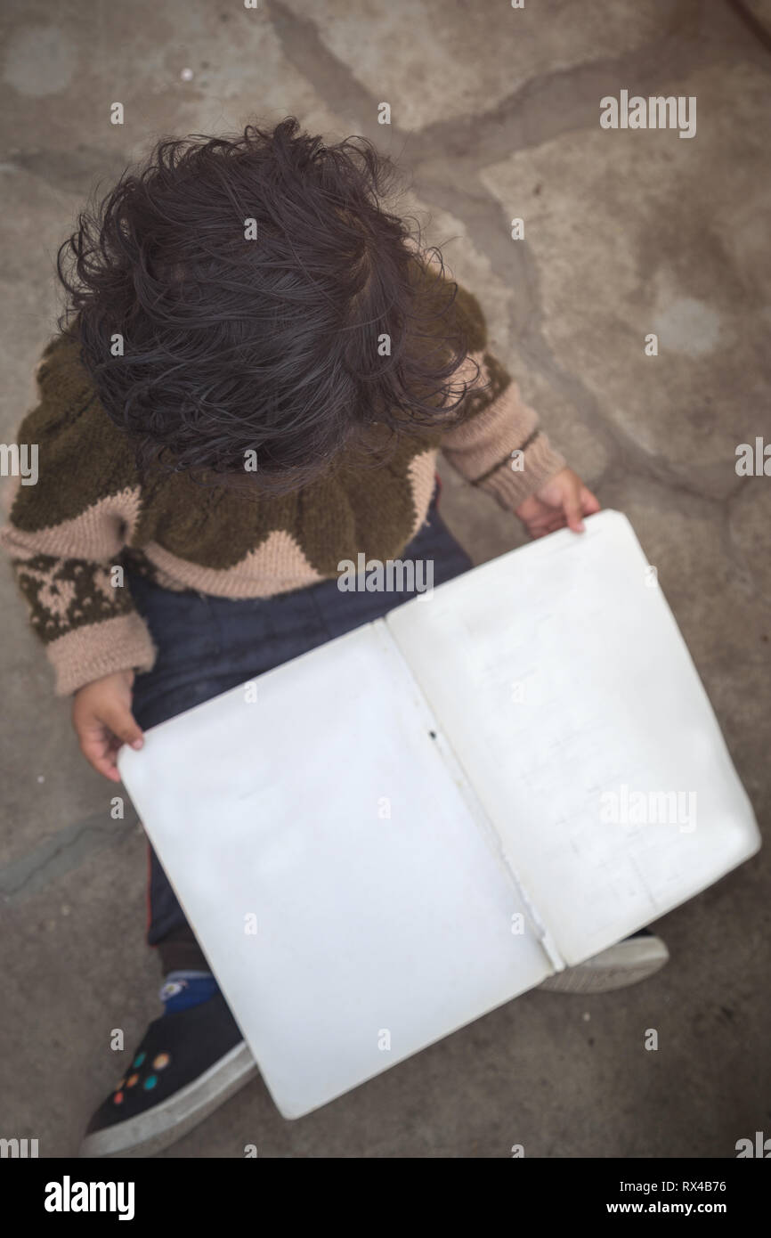 Angolo di Alta Vista della Cute 2 anno little indian Asian Baby girl kid con il Libro bianco mentre è seduto sul pavimento. Foto Stock