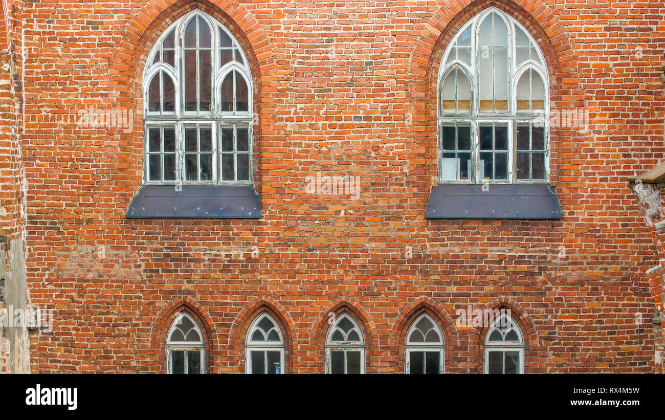 Il rosso la parete in mattoni vecchio edificio. Si tratta di una vecchia chiesa del periodo medievale con le rovine si vede sulla parete Foto Stock