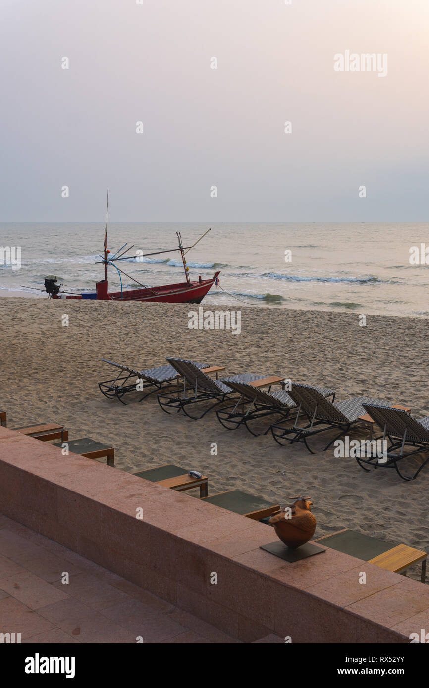 Thai long tail barca da pesca e sedie resort sulla spiaggia di una bella mattina di sunrise. Foto Stock