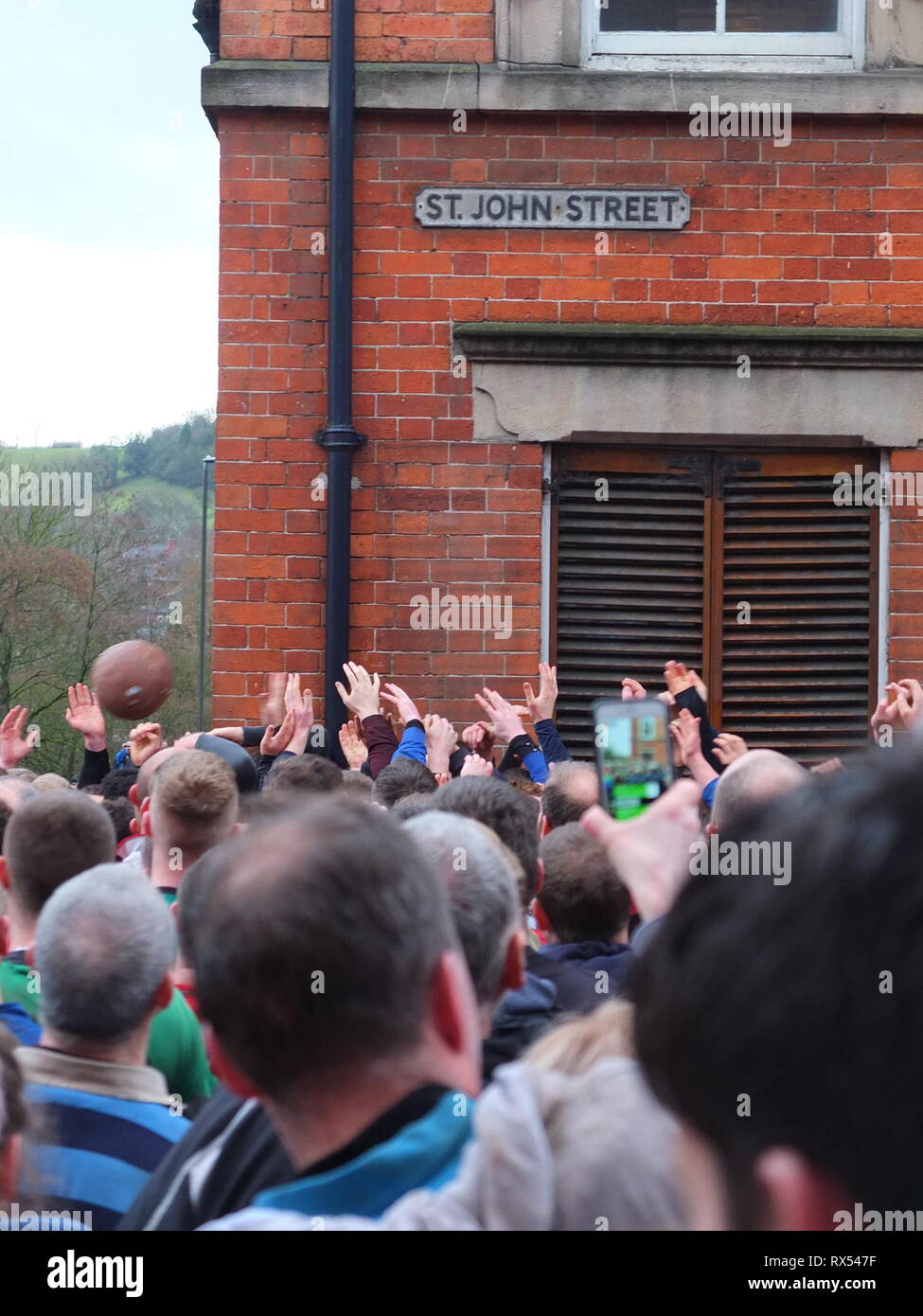 Ashbourne Shrovetide Football 2019. Le mani in un mare di giocatori afferrare per la palla su St John Street come giocare entra in città durante il Mercoledì delle Ceneri gioco. Foto Stock