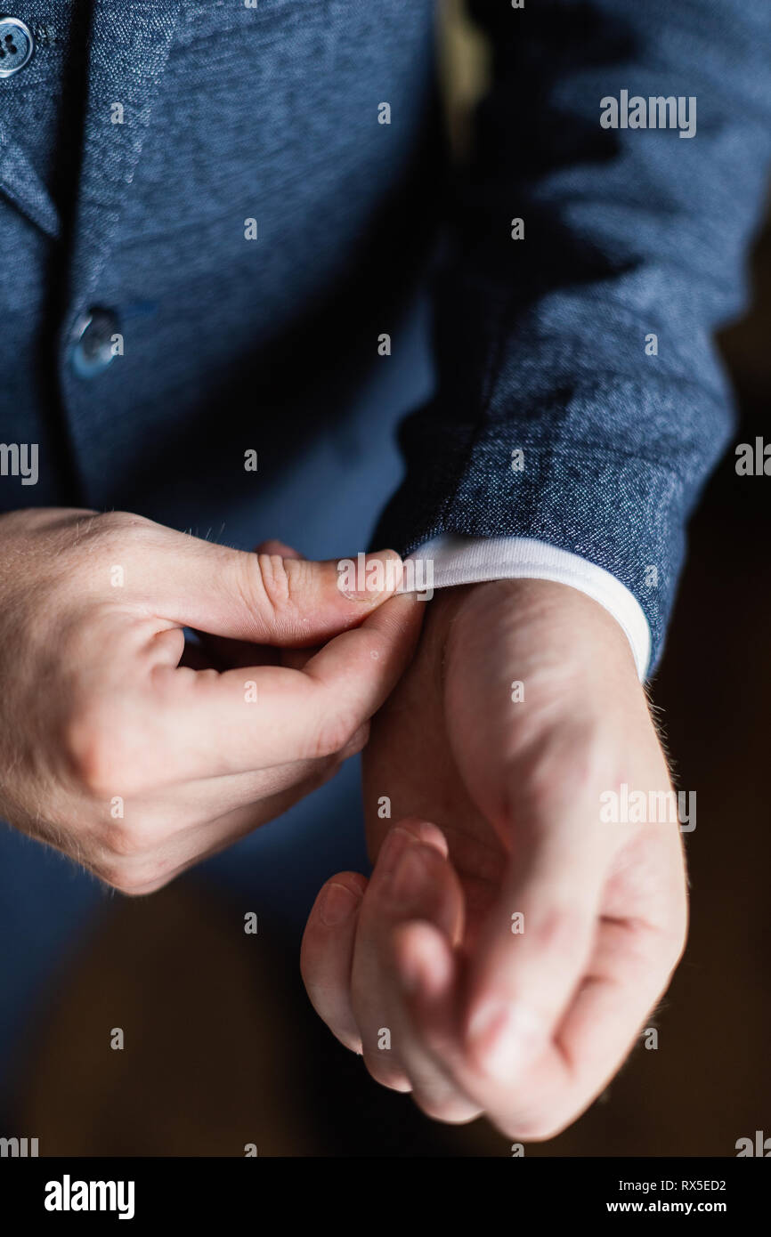 Imprenditore in una camicia bianca si raddrizza polsini, in piedi presso la finestra nella luce naturale. Uomo bracciale pulsanti-link sul francese polsini maniche bianche di lusso Foto Stock