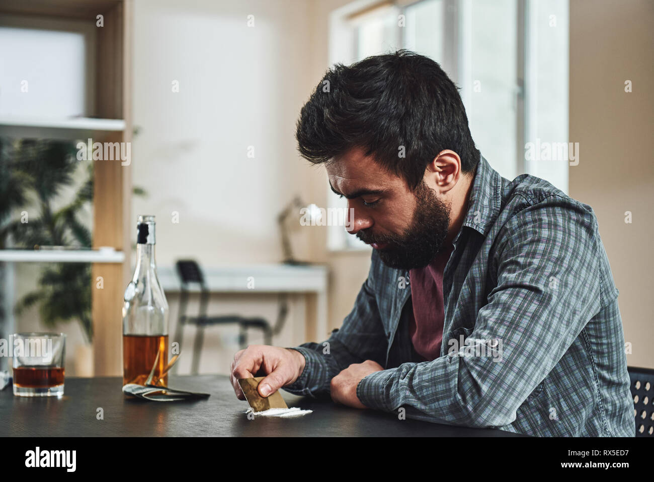 Premuto barbuto uomo si siede a tavola si prepara a snort una linea di cocaina tramite banca nota. Egli soffre di problemi sul lavoro e difficoltà in r Foto Stock