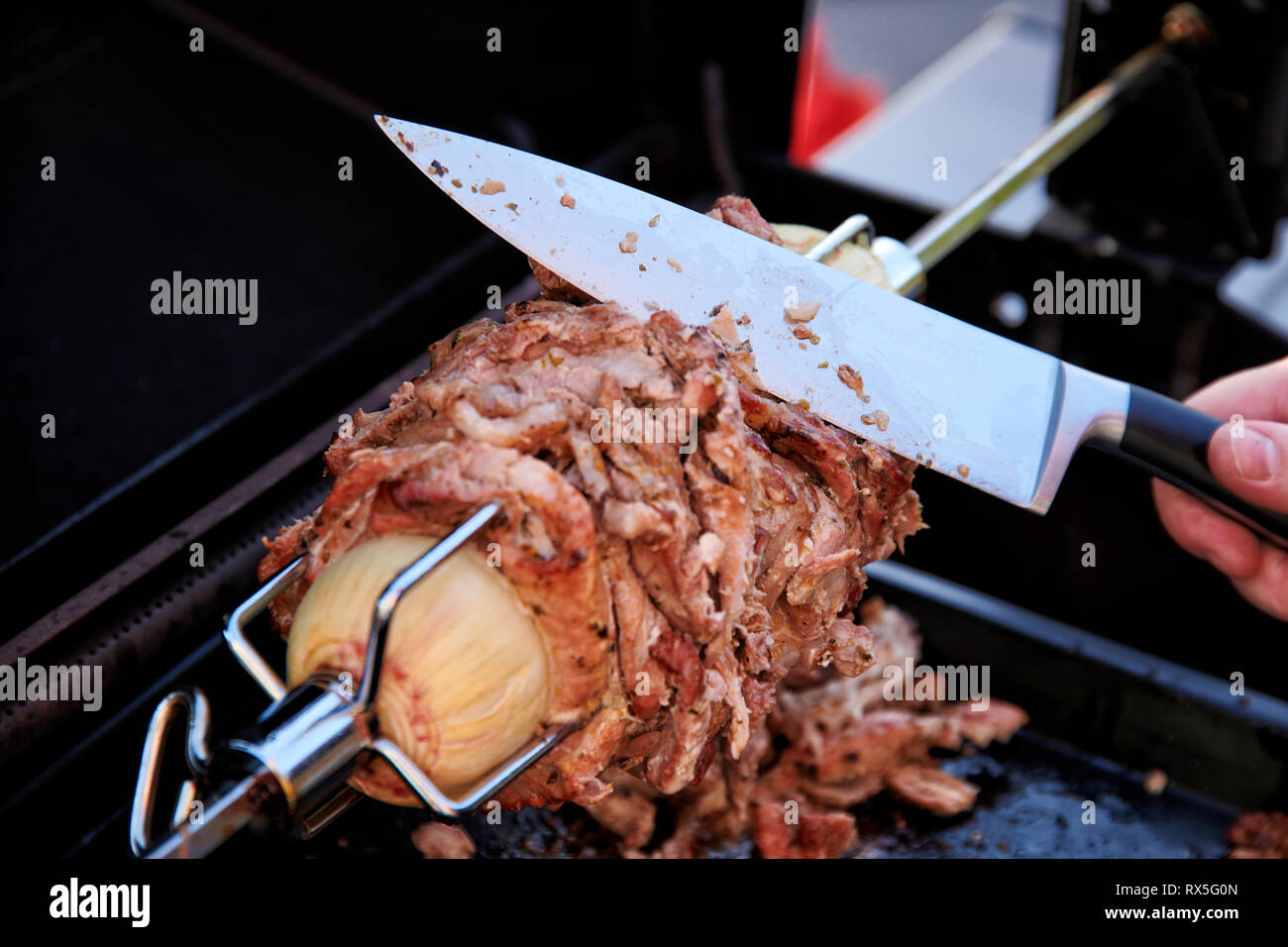 Von einem selbstgemachten Doenerspiess der in einem Grill eingespannt ist, wird Mit einem grossen Messer eine porzione abgeschnitten. Foto Stock