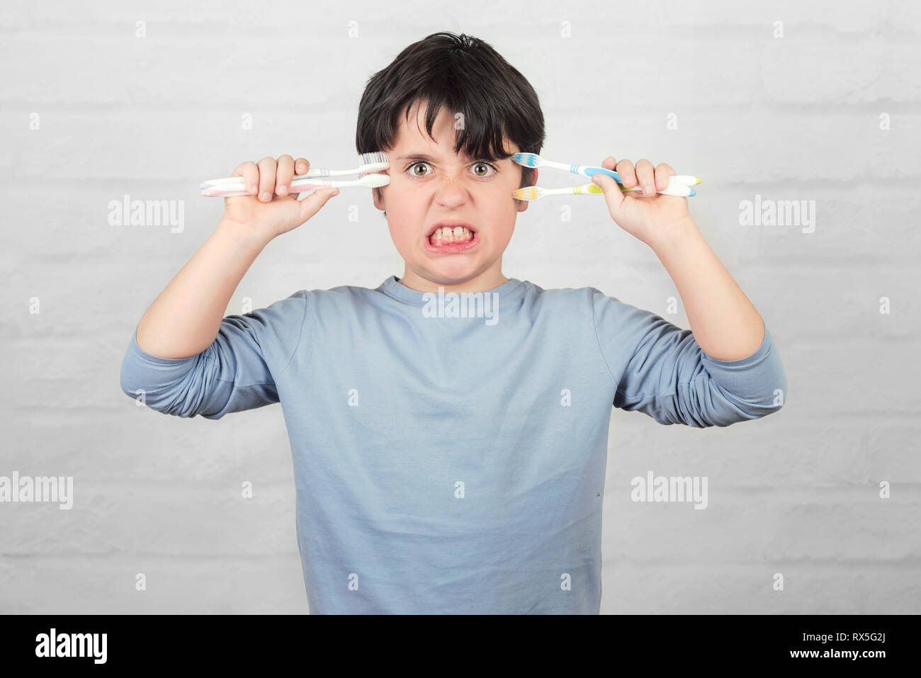 Arrabbiato ragazzo che non si desidera pulire i suoi denti contro Sfondo mattone Foto Stock