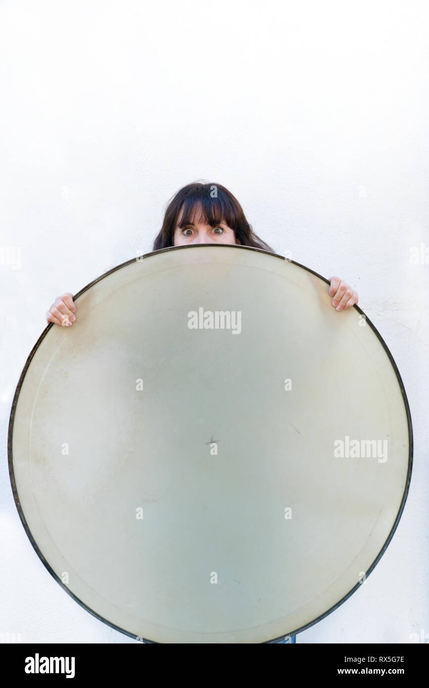 una donna bruna francese si nasconde dietro un coperchio a tamburo circolare con solo le mani e uno sguardo spaventoso negli occhi Foto Stock