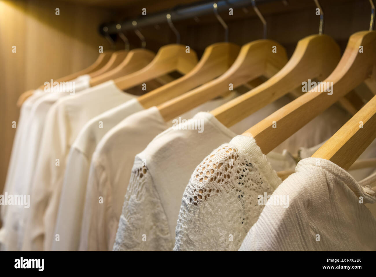 White bluse e maglioni su appendiabiti in un armadio con illuminazione. Close-up. Foto Stock