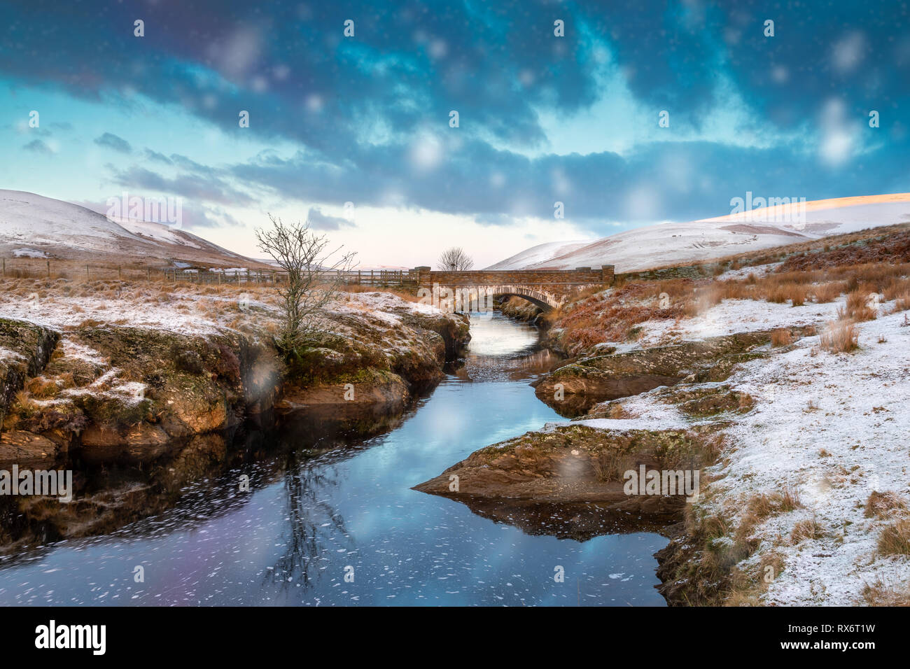 Pont Ar Elan, Elan Valley, il Galles. Snowy scena di Afon elan che scorre sotto un ponte con Lone Tree e early sun Foto Stock