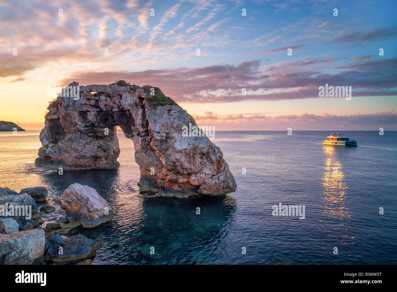 Es Pontas in Mallorca con barca ancorata nelle vicinanze del mare Mediterraneo. Sunrise con sun glinting off lo yacht e rock arch. Foto Stock