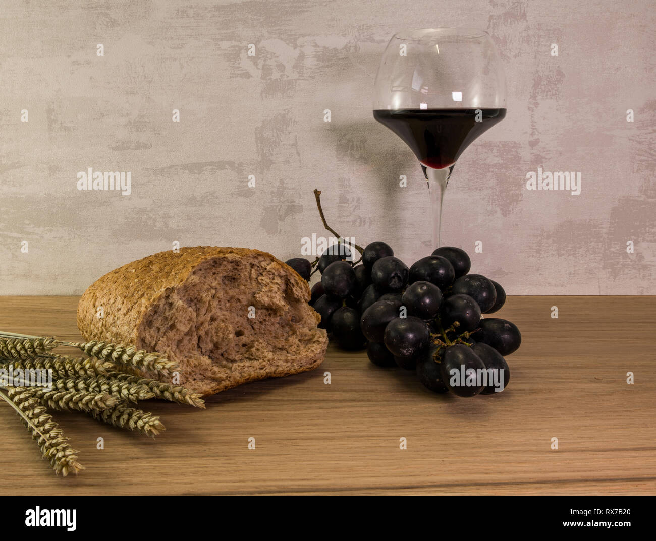 Un pane di frumento e shock di grano con uve rosse e bicchiere di vino rosso come sfondo di pasqua Foto Stock