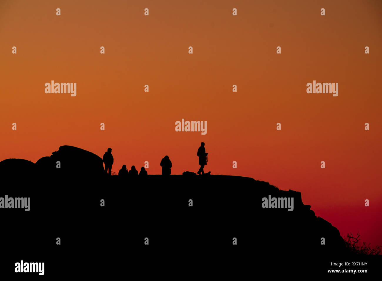 Silhouette di persone sulla cima di una montagna al tramonto con il cielo rosso Foto Stock