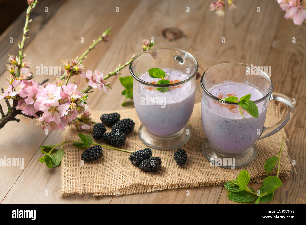 Frutta fresca frullato frullato di blackberry, viola o yogurt gelato drink sulla tavola di legno con ciuffi di menta, more e fiori di ciliegio. Foto Stock