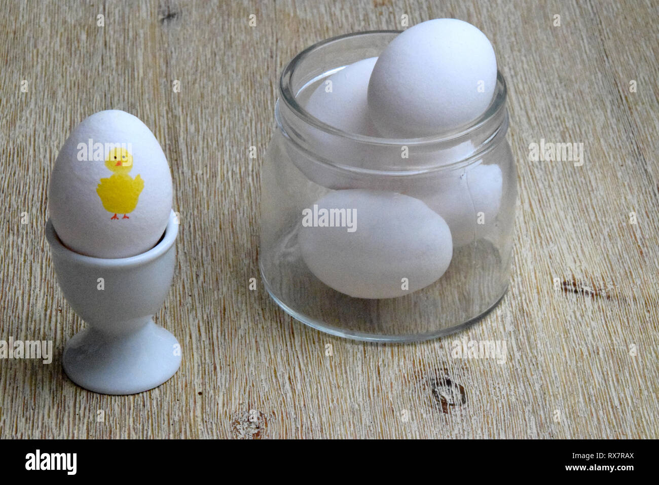 Uova in recipiente di vetro e uova sode con un giallo di pollo di Pasqua dipinto su di esso Foto Stock