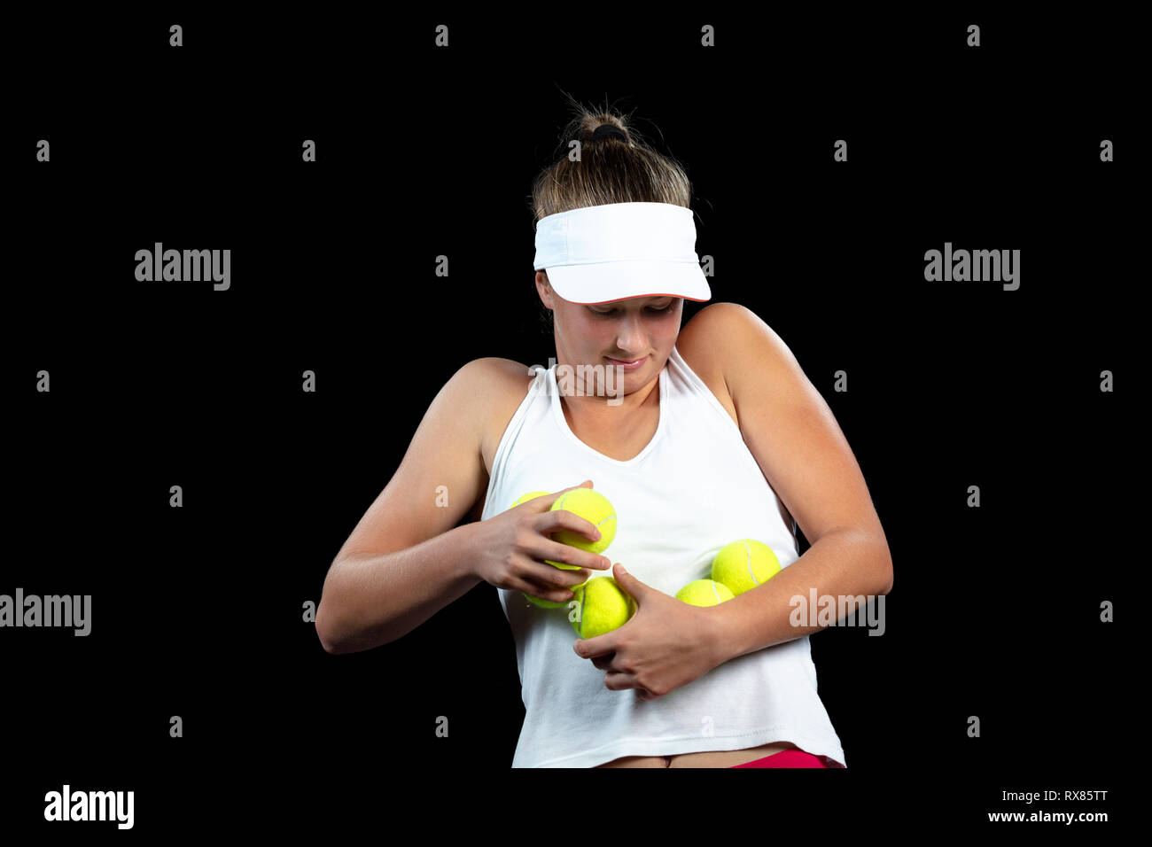 Giovane donna su una pratica di tennis. Giocatore principiante tenendo un racket, apprendimento delle competenze di base. Ritratto su sfondo nero. Foto Stock