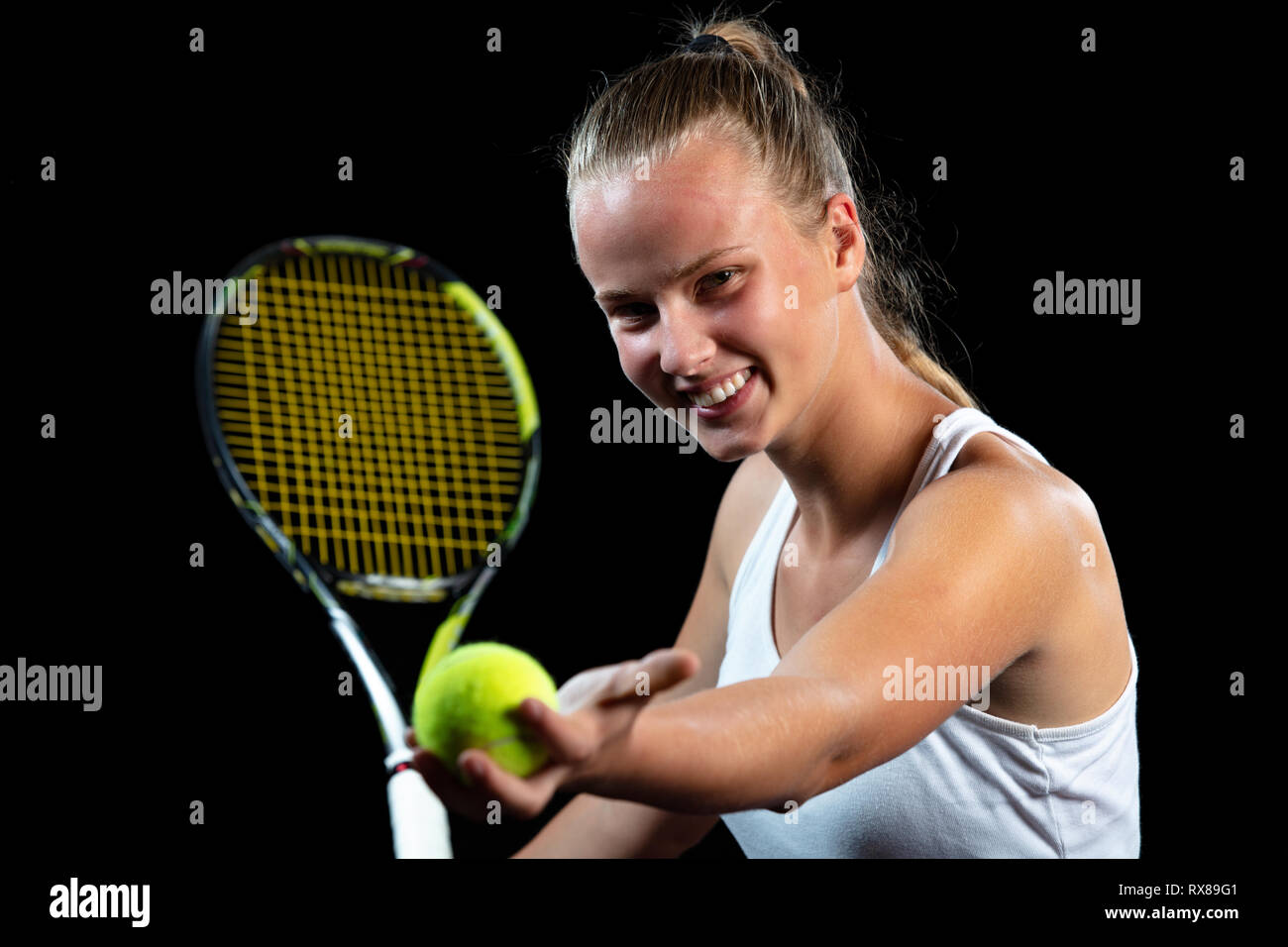 Giovane donna su una pratica di tennis. Giocatore principiante tenendo un racket, apprendimento delle competenze di base. Ritratto su sfondo nero. Foto Stock