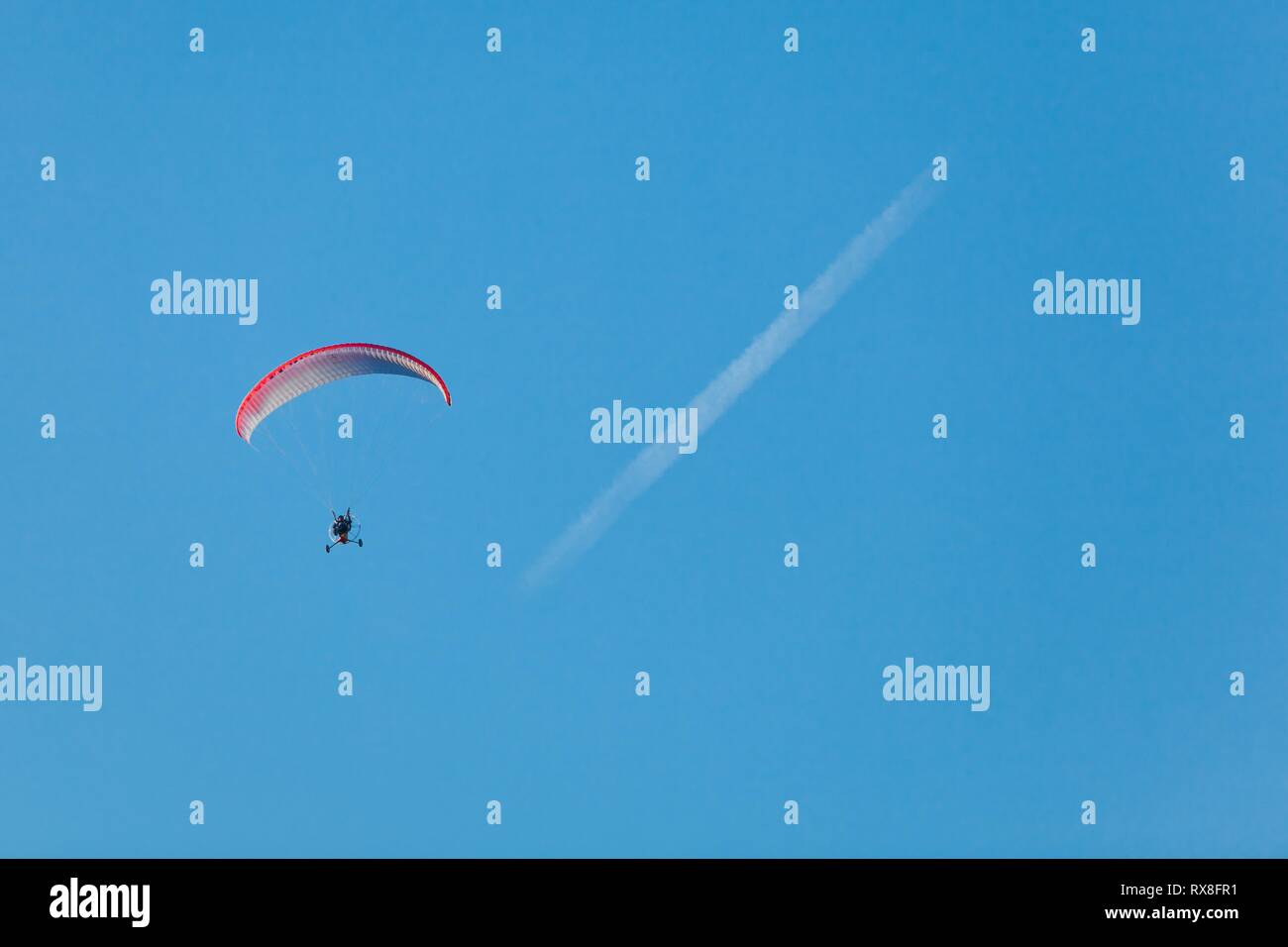 Parapendio volare nel cielo sopra lo sfondo blu dove è la condensazione traccia visibile. Modi di trasporti aerei. Foto Stock