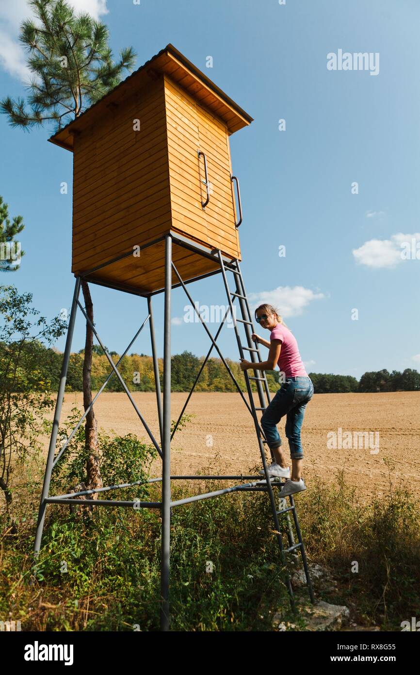 Donna salendo sulla seduta alta per cacciatori con base in acciaio e piano in legno. Giornata di sole. Foto Stock