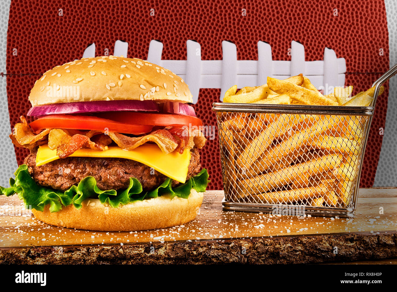 Cheeseburger con pancetta e un cestino di patatine fritte. Sfera di calcio immagine in background. Foto Stock