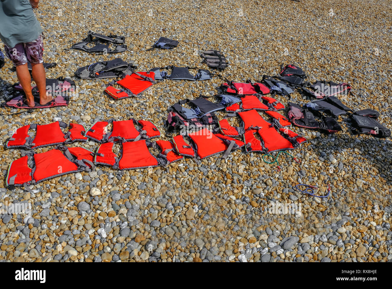 Fila di bambini rosso di giubbotti di salvataggio allineate su una spiaggia di ciottoli. Usato per la vela e il surf lezioni di imbarco. Foto Stock