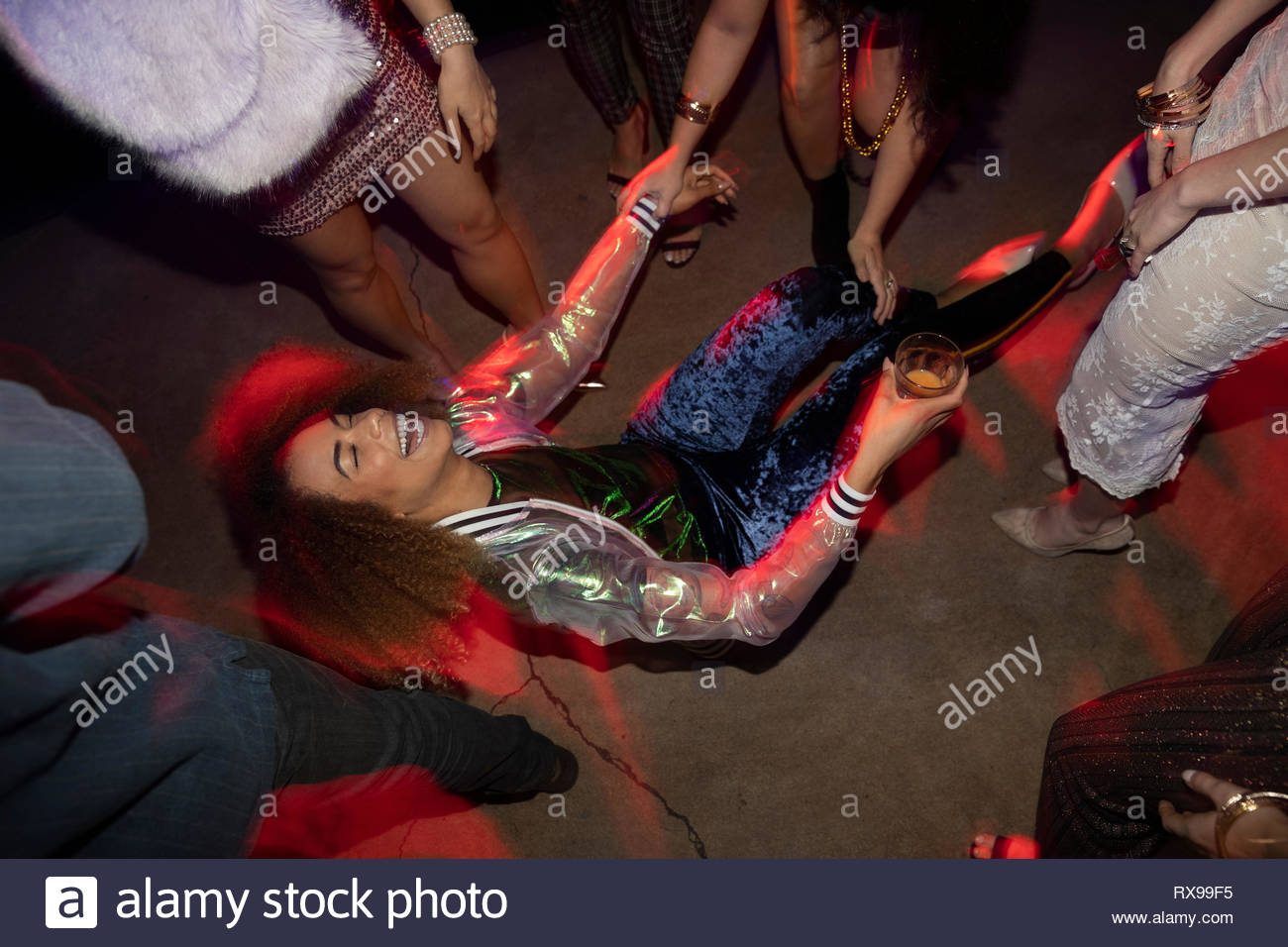 Ridendo giovane donna cadere sulla pista da ballo in discoteca Foto Stock