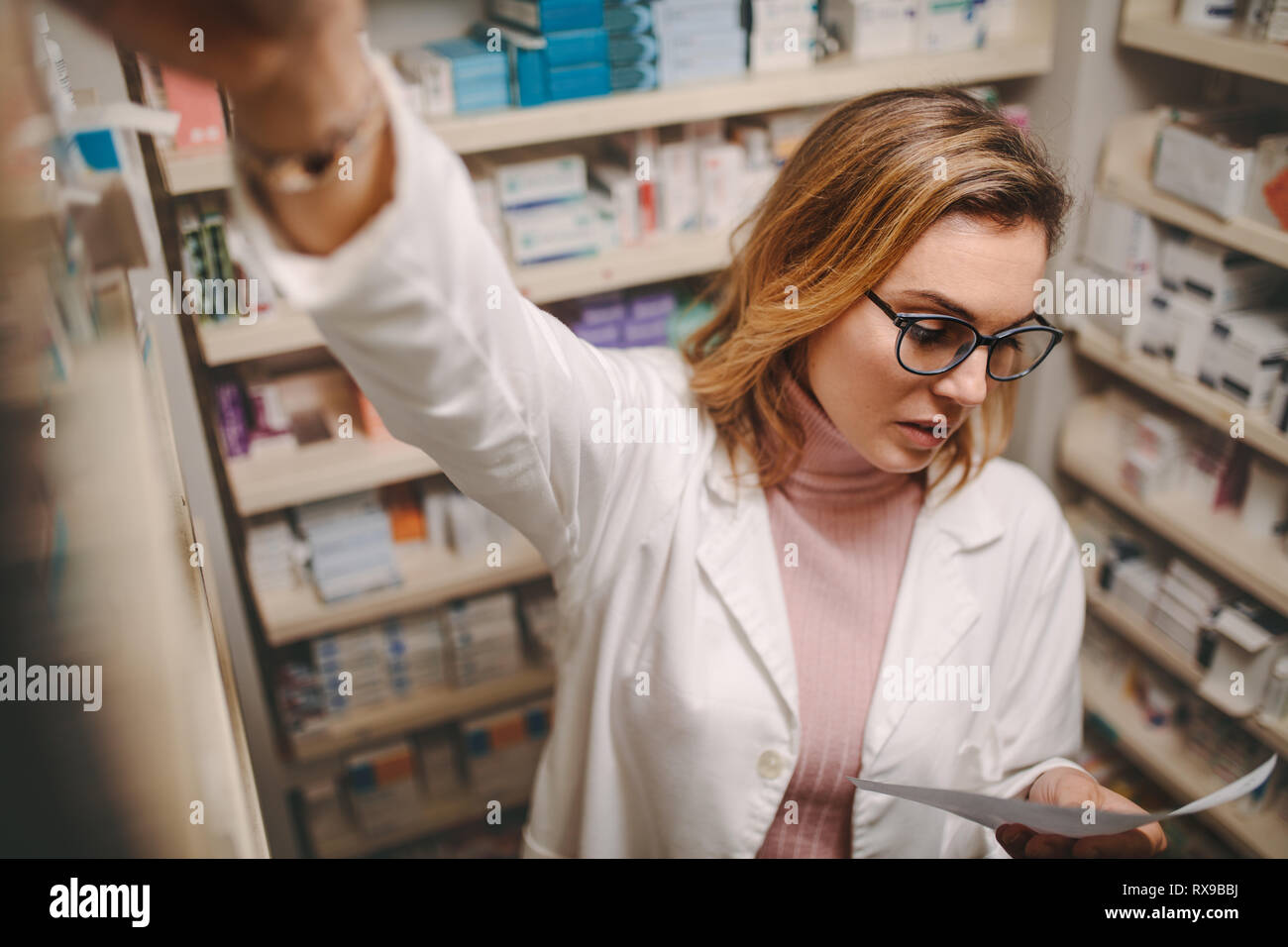 Il farmacista femmina azienda ricerca la prescrizione di medicine in farmacia store. Farmacia guardando la prescrizione durante la ricerca farmaco prescritto sul ripiano Foto Stock