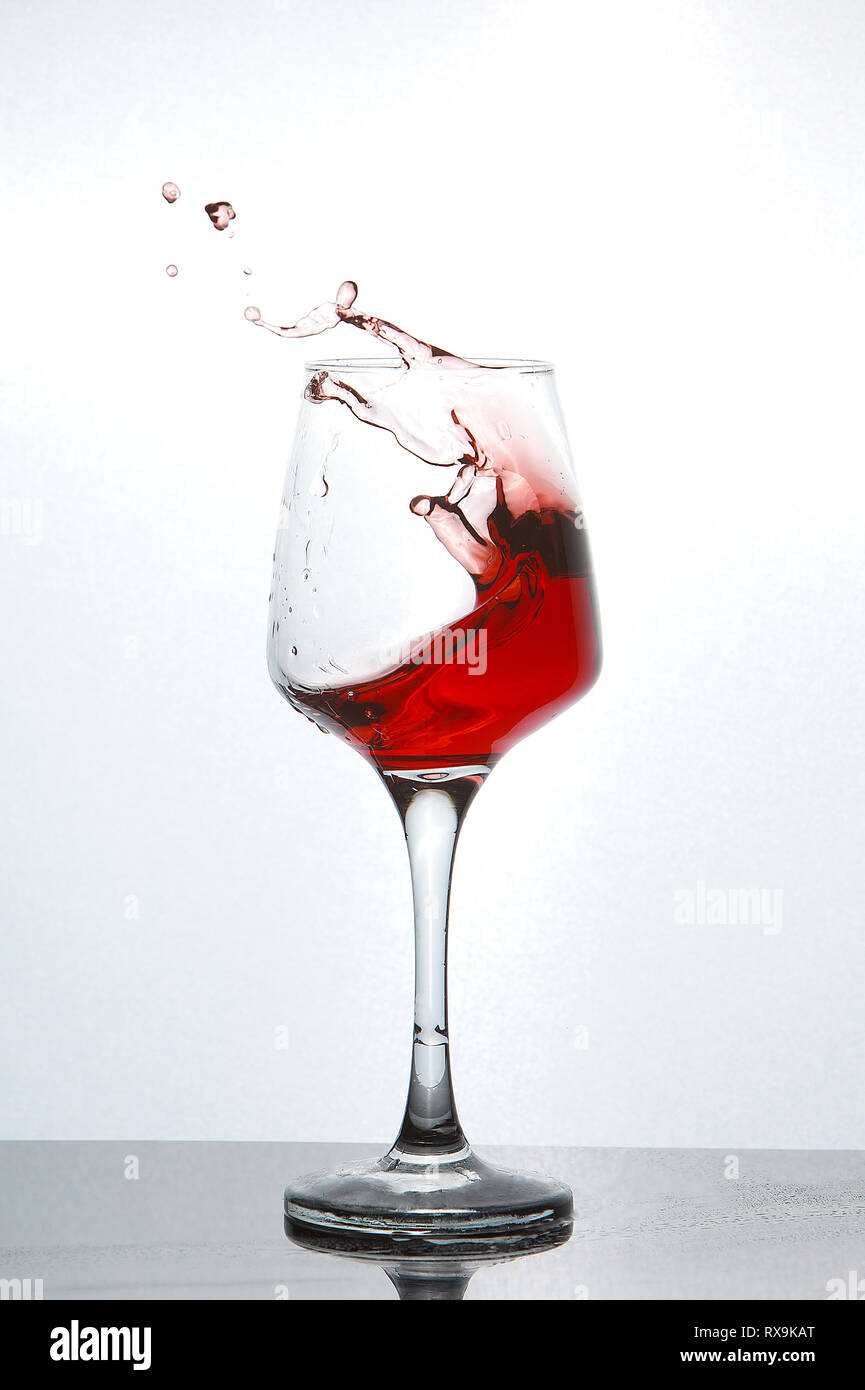 Close-up di vino rosso schizzi in vetro sulla tavola su sfondo bianco Foto Stock